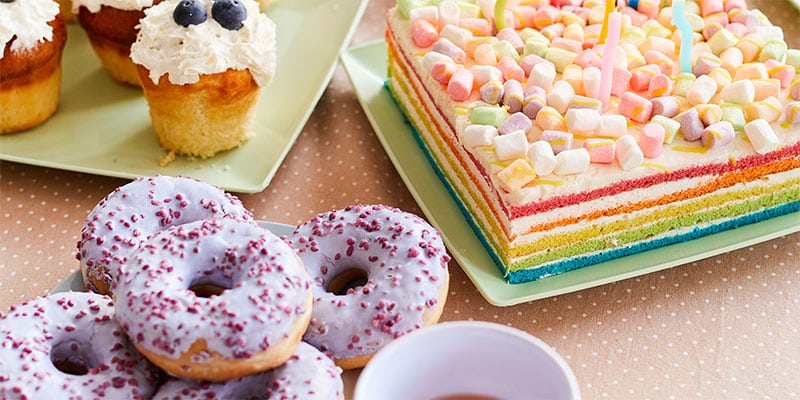 Donut-themed first birthday dessert table featuring a variety of treats, including a donut cake, cupcakes, and a colorful birthday cake topped with marshmallows.