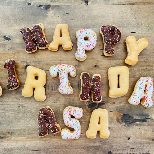 Happy birthday spelled out in sprinkle-covered donuts with the name Asa on a wooden background.