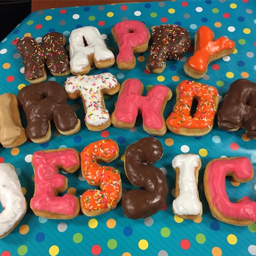 Happy birthday Jessica spelled out in colorful frosted donuts with sprinkles, arranged on a polka-dotted tablecloth.